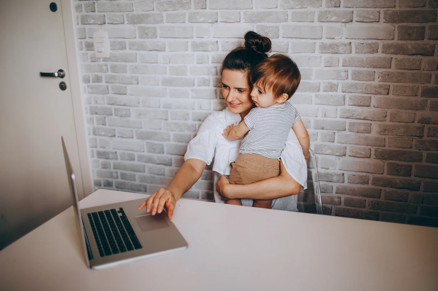 Mãe trabalha no computador com o filho pequeno no colo