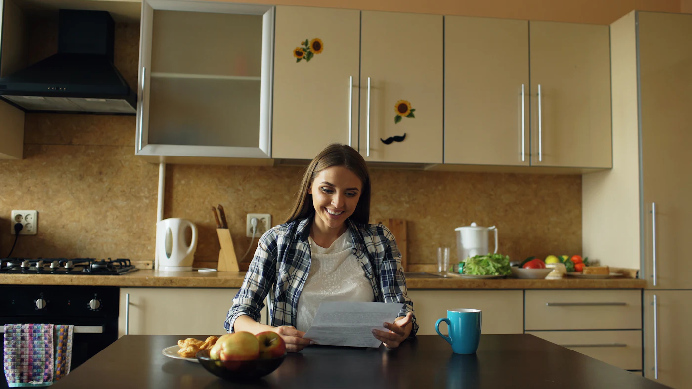 Mulher lê uma carta sentada à mesa da cozinha