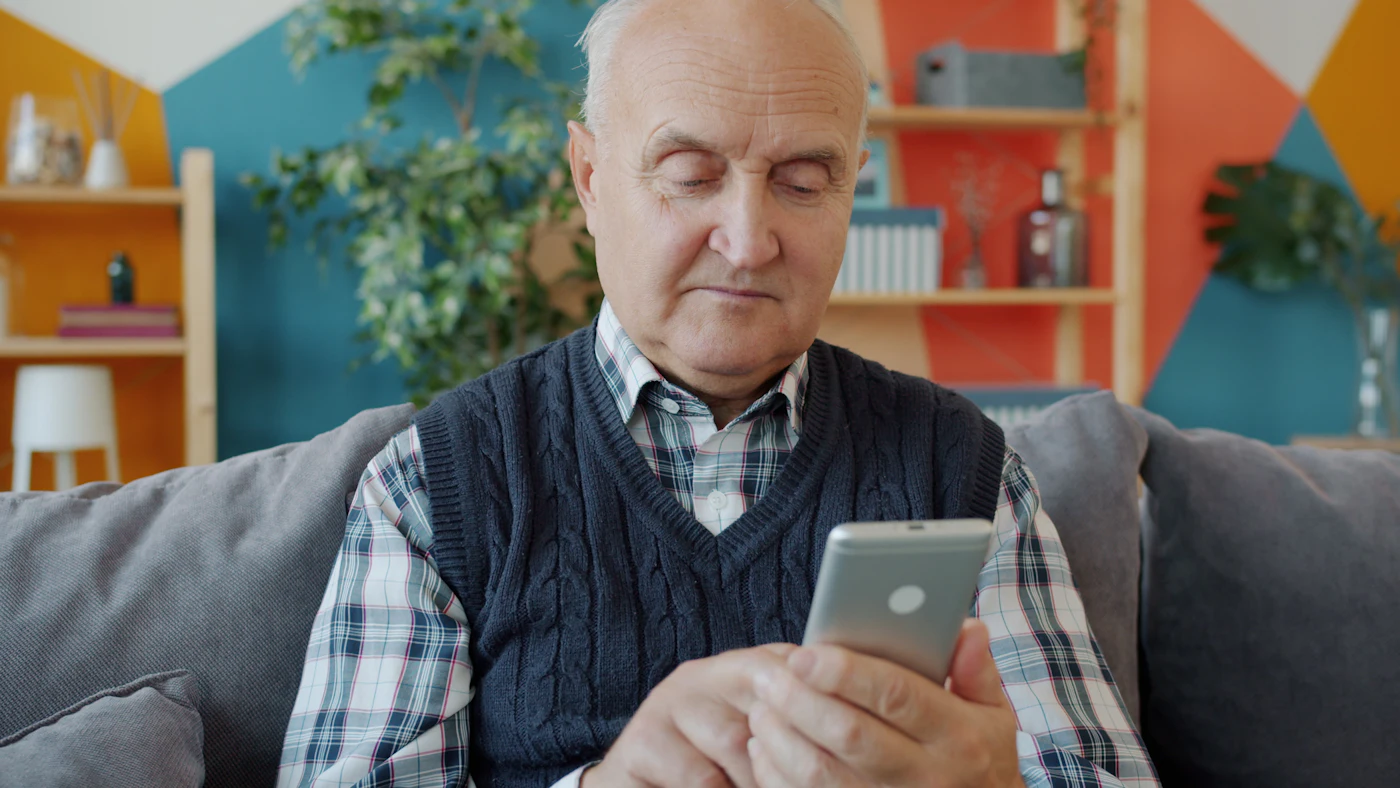 Homem idoso olha a tela do celular sentado no sofá