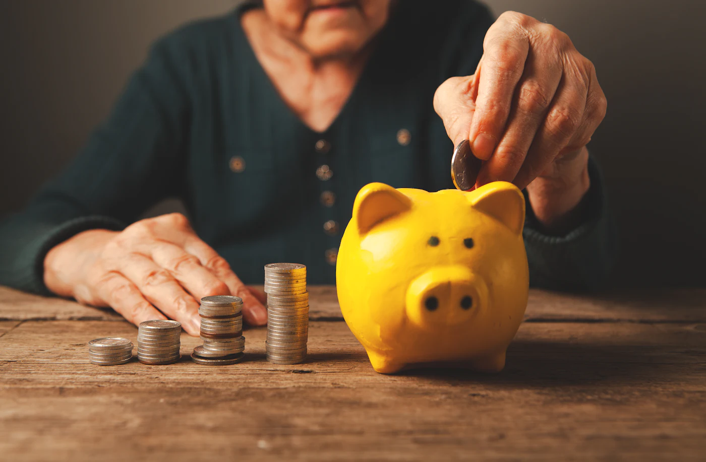 Mãos de uma pessoa idosa colocam moedas em um cofrinho