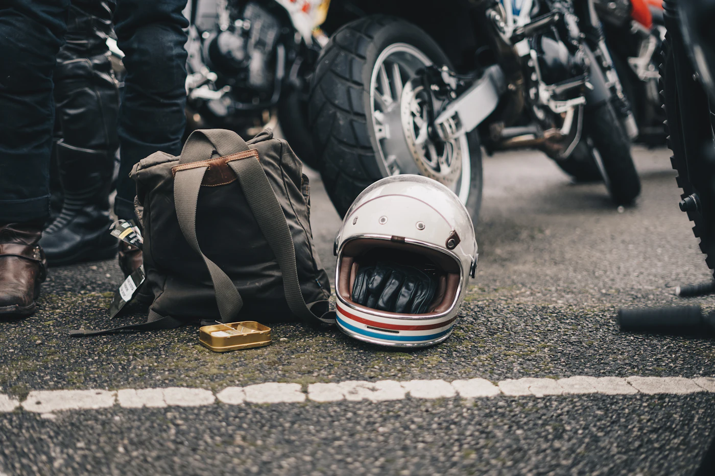 Capacete branco no chão ao lado de uma mochila, perto de motos estacionadas