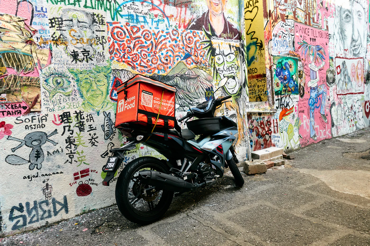 Moto de entrega com bolsa térmica estacionada junto a um muro grafitado